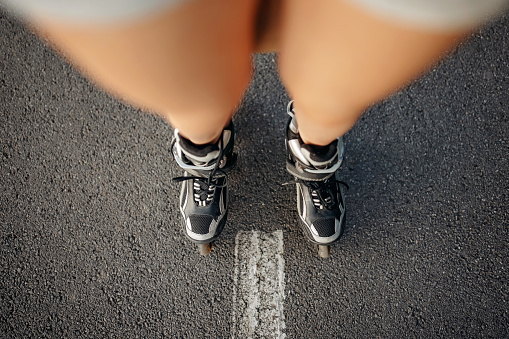 A Caucasian woman wearing rollerskates, standing on the road, with the accent on the skates.