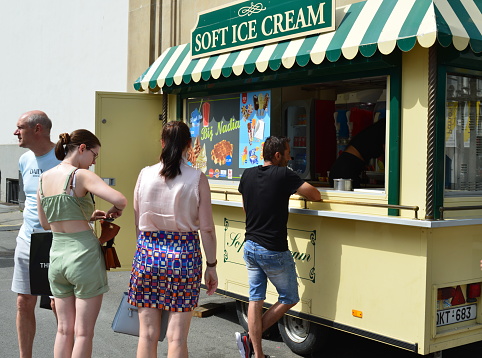 Antwerp city, Province Antwerp, Belgium - June 18, 2022: passers-by  caucasians 2 adult men and  women in the street stop at an ice cream vintage truck to order an ice cream with such a warm late spring Saturday morning
