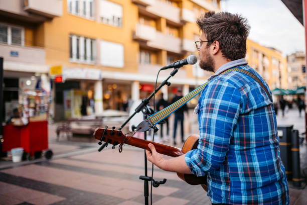 Handsome young male guitar player singing and playing a guitar on the city square.