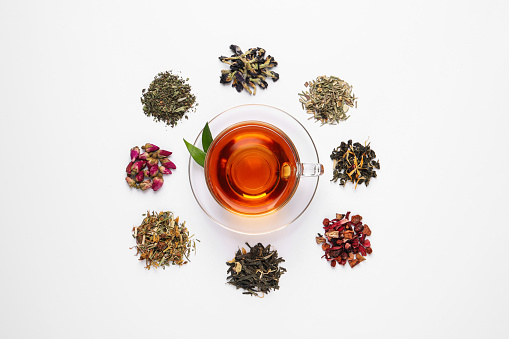 Composition with brewed tea, dry and fresh leaves on white background, top view