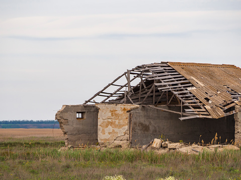 An abandoned collapsed building on the prairie. Collapsed walls and a falling roof on the building. A ghost town. A large destroyed shed-hangar