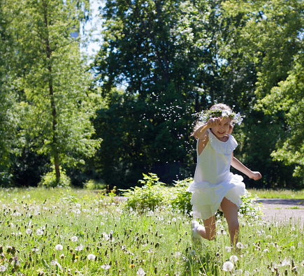 little girl in a straw hat with an apple in her hand runs through the forest at sunset. A happy child, a girl runs through the green grass. A child running through a field of flowers.