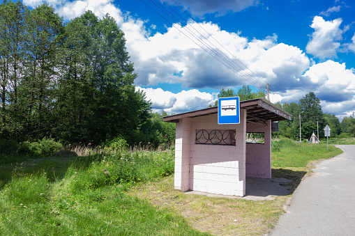 Bus stop on the side of a road in countryside. Station is empty on sunny summer day with beautiful sky on background. Rural landscape