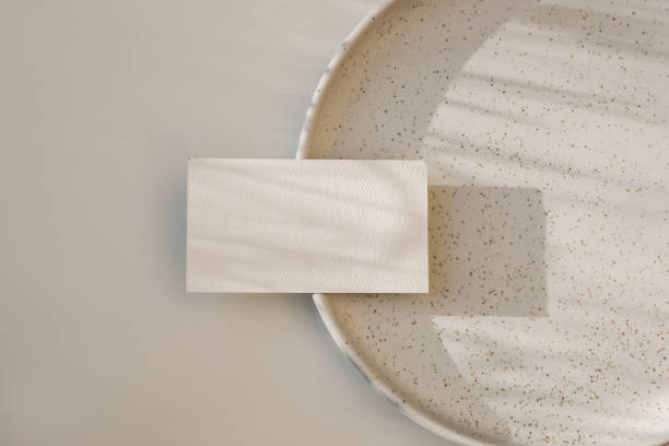 Modern neutral branding stationery. Closeup of textured blank business card, invitation mockup on dotted, speckled ceramic plate in sunlight. Beige table background, flat lay, top view. No people. papelería moderna de marca neutral. primer plano de la tarjeta de visita en blanco texturizada, maqueta de invitación en una placa de cerámica punteada y moteada a la luz del sol. fondo de mesa beige. tendido plano, vista superior. no hay gente.