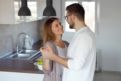 An affectionate young couple dancing together in their kitchen at home