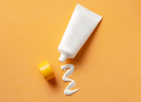 Mockup of White cosmetic tube with sunscreen cream and squeezed cream texture on orange background. Top view