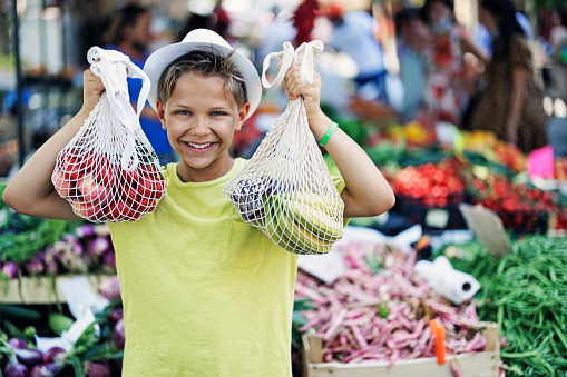 Teenage boy buying groceries at the farmer's market. The boy is using reusable bags.\nCanon R5