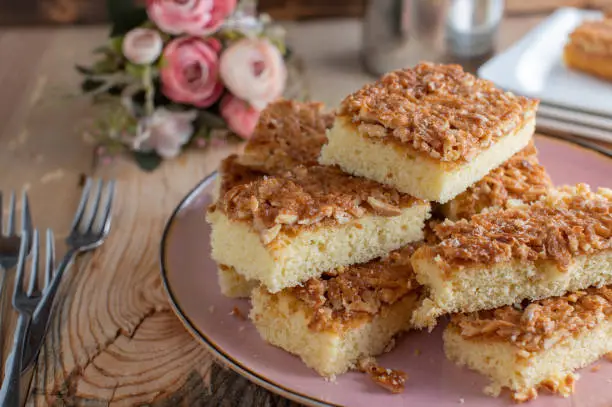 Delicious sheet cake recipe with a sponge cake and caramelized almond topping. Served stacked on a plate on wooden table.