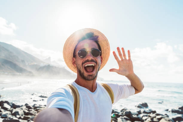istock Young man with backpack taking selfie portrait outside - Smiling happy guy enjoying summer holidays at the beach - Millennial showing victory hands symbol to the camera - Youth and journey 1404212683