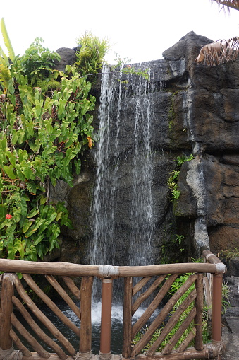 Small waterfall in tropical surroundings with wooden bridge.