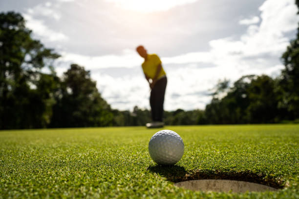 golfista che mette la palla sul campo da golf verde, bagliore della lente al tramonto serale. - short game foto e immagini stock
