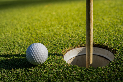 Elija el enfoque. Una pelota de golf blanca cerca del hoyo de golf y un asta de bandera sobre hierba verde. photo