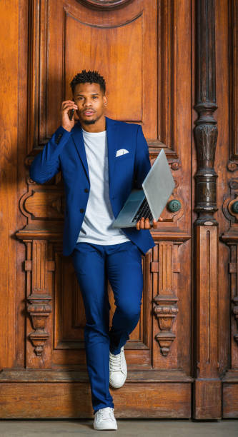 istock Young man talking on cell phone,  working on laptop computer, standing by office door in New York City 1404216587