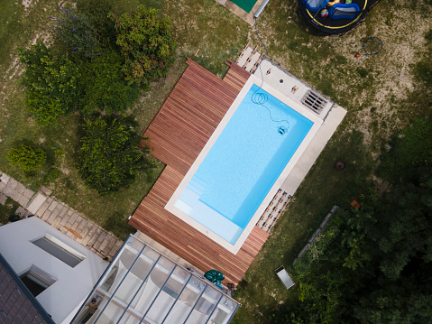 aerial drone flight over beautiful green garden with pool and the wooden deck of the pool is in progress and pool robot is working right now in the water