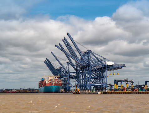 A massive Maersk Line container ship being manoeuvred into position by the quayside at Port of Felixstowe, Suffolk, Eastern England, by tug boats where, once safely moored, the containers will be lifted by the cranes onto waiting lorries. Port of Felixstowe is the busiest container port in the UK.