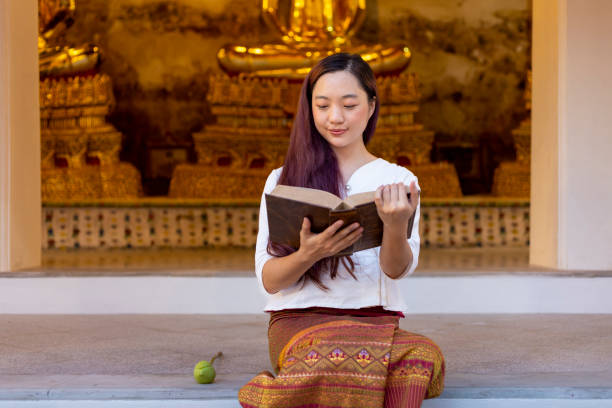 una donna buddista asiatica sta leggendo l'antico libro tripitaka sanscrito dell'insegnamento del dhamma del signore buddha mentre è seduta nel tempio per cantare e adorare nel monastero - buddha thailand spirituality wisdom foto e immagini stock