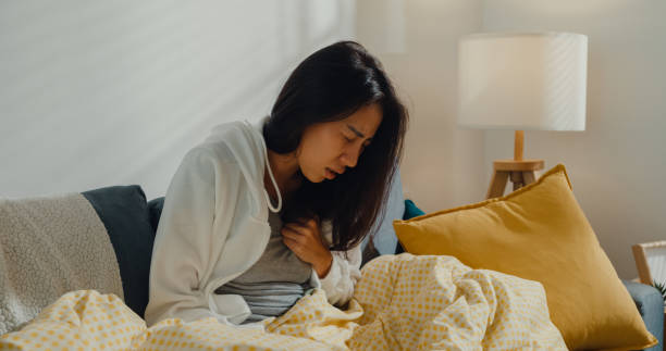 больная молодая азиатская женщина, перенесшая сердечный приступ, сидит на диване в гостиной дома. - house burning color image danger стоковые фото и изображения