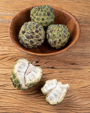 Sugar apples or custard apples in a bowl with cut fruit over wooden table.