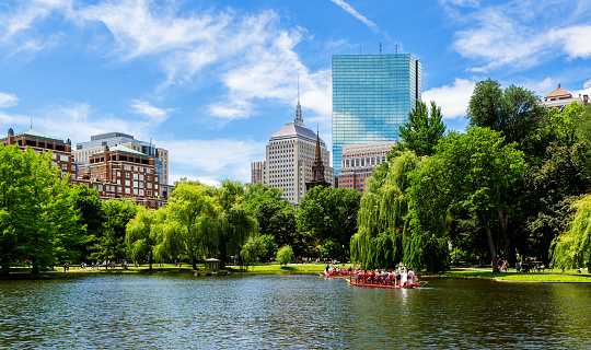 Boston, Massachusetts, USA - June 18, 2022: Boston Public Garden pond with a swan boat and Back Bay buildings in the background.