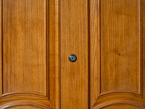 A peephole in the center of a beautiful wooden vintage door with a light texture.