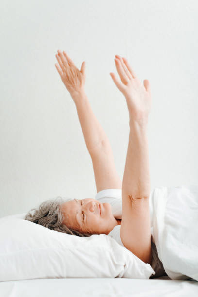 istock Smiling awake senior woman stretching after sleeping while lying in bed in bedroom. Side view mature woman relaxing enjoying waking up in morning 1404235844