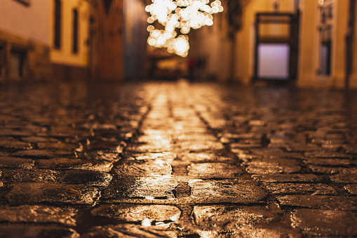 Wet cobblestone footpath in old town. Lights reflecting in cobble road after rain