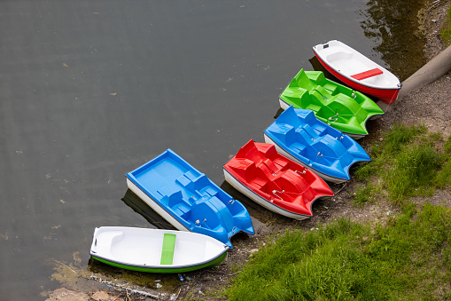 Bright plastic boats and catamarans for rental on river bank. Parking of catamarans for walks on boat station. Active summer holiday. Top view
