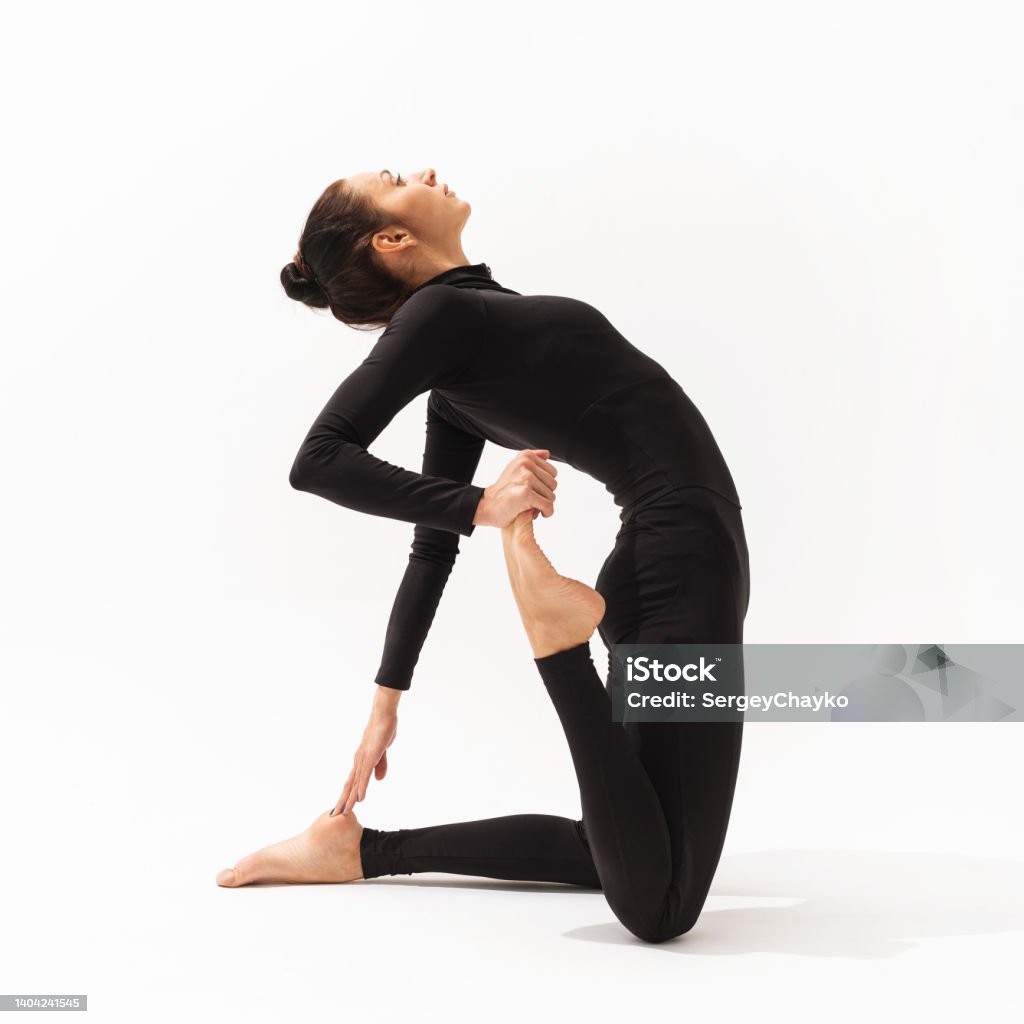 A woman in black sportswear practising yoga performs an exercise of Ushtrasana with Virasana, a camel and hero pose on a white background Exercising Stock Photo
