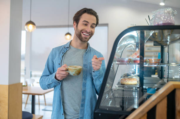istock Man with coffee pointing at food display 1404243015