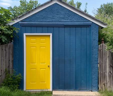 Blue backyard shed with bright yellow door.