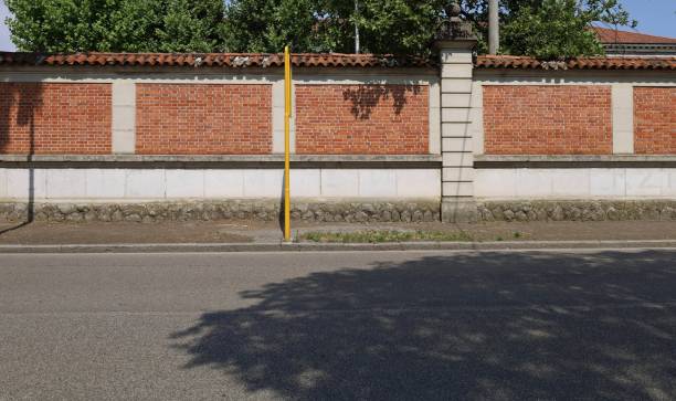 istock Brick wall with columns and lower side made of bricks. 
Sidewalk, yellow pole and asphalt street in front. 1404244891