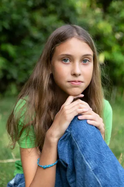 Young girl with green or blue eyes outdoors, looking strait forward to the camera. Shy look. Introspective. Not smiling