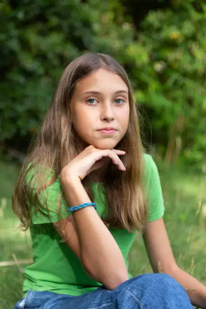 Young girl with green or blue eyes outdoors, looking strait forward to the camera. Shy look. Introspective. Not smiling