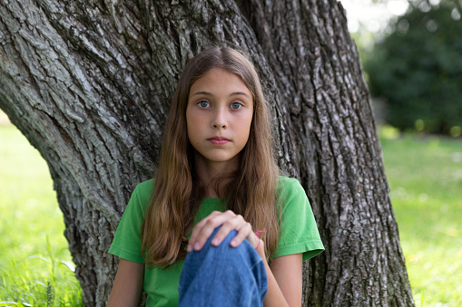Young girl with green or blue eyes outdoors, looking strait forward to the camera. Shy look. Introspective. Not smiling