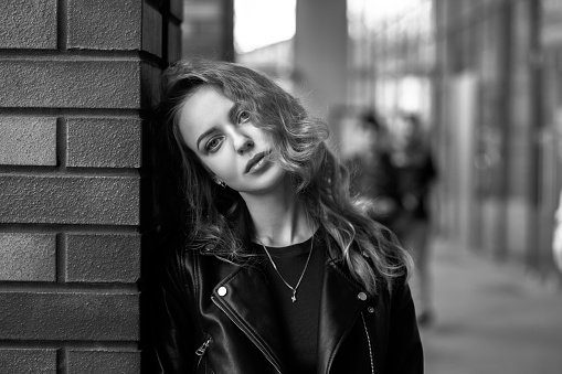 sad serious blond woman in leather coat stand on street looking at camera, monochrome