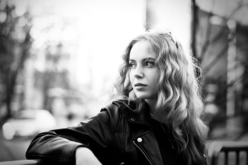 sad serious blond girl in leather coat on street looking aside, monochrome
