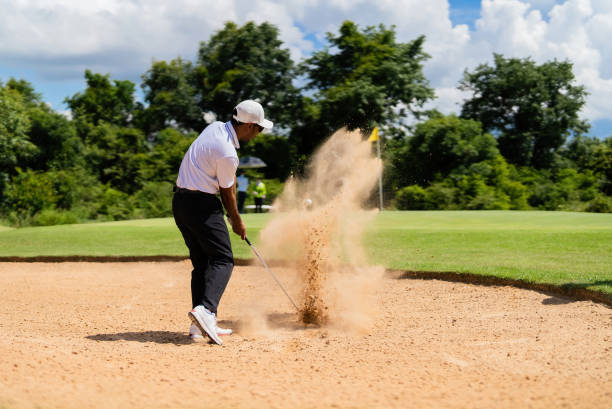 istock Asian man golfing on the course. He hits a golf ball on a sand field. 1404245883