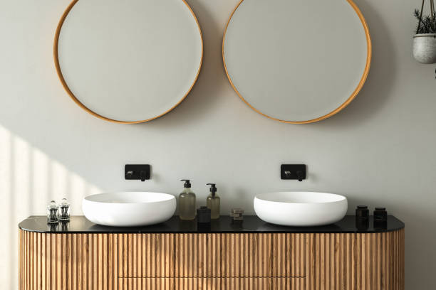 istock Close up of double sink with oval mirrors standing in on grey wall 1404248352