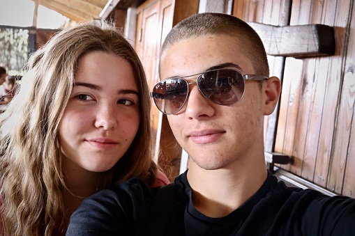 younger sister and older brother with sunglasses sitting together in cafe