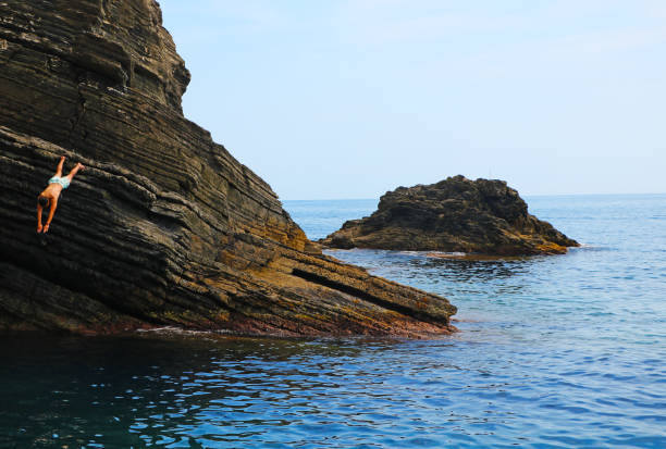 Vernazza, Cinque Terre, La Spezia, Liguria, Italy - June 15, 2022: the photo was taken in Vernazza, one of the Cinque Terre, on a clear day at the end of spring. It shows its beautiful and mighty rocks and a man dipping in the water from one of them.