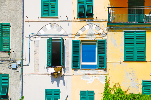 Portovenere, La Spezia, Liguria, Italy - June 16, 2022: the photo was taken in a clear day of end of spring, and shows the windows of a beautiful facade, with arch decorations, facing the harbor of Portovenere. From one of the windows, a laundry is hanging out in the sun.