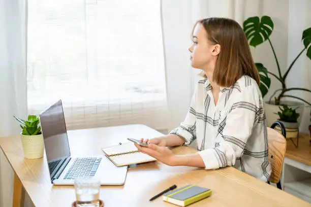 Photo of Young woman working on laptop at home. Cozy home office workplace, remote work, e-learning concept.