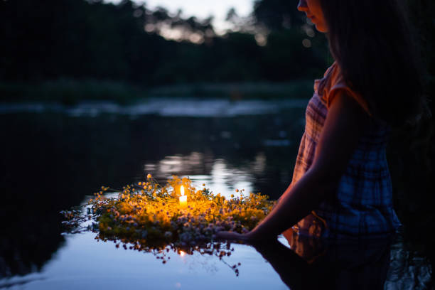 Girl holding wreath with burning candle, setting it to flow on the river, making a wish