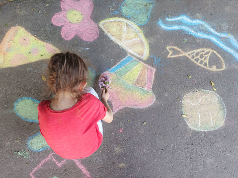 A child drawing in chalk on concrete asphalt.