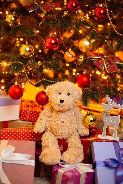 istock Cute teddy bear sitting on presents under Christmas tree 1404259107