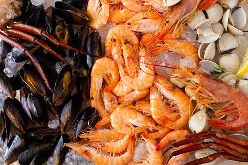 Overhead shot of a selection of seafood and shellfish on ice with lemon. Including fresh mussels, clams, crab,  shrimp, and langoustine. Stock photo.