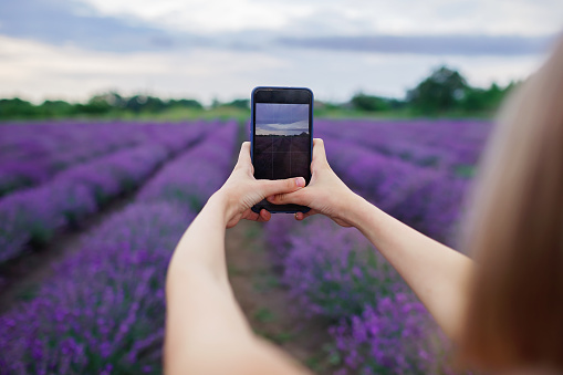 Close-up of screen of mobile phone in the hands. Teenage girl enjoys lavender field and makes photo with smartphone. Walk in purple flowers at sunset. Beauty of nature, summer travel and vacation