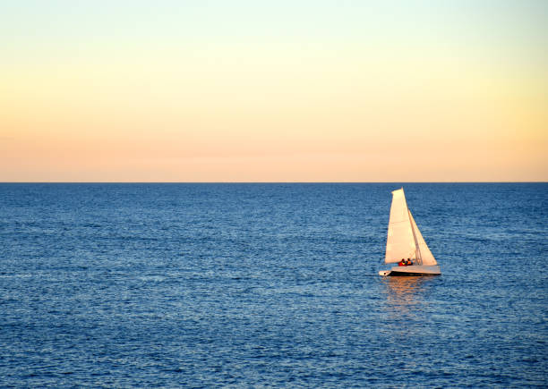 Sailboat at sea on sailing on the waves. Yachtsman during training on a sailboat. Skiff and Sailboat in sea port near the Spanish coast. Sail sport in Yacht club. Sail boat on waves on sunset in sea.