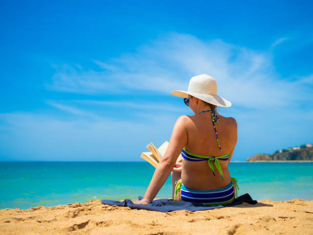 Beautiful woman reading book sitting on beach stock photo