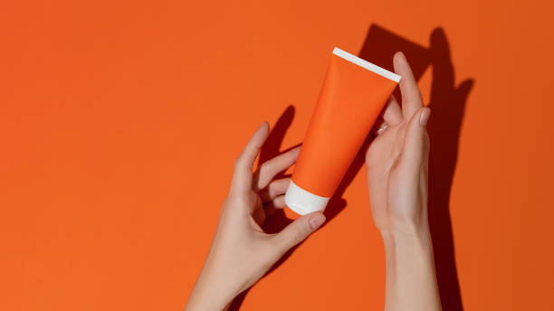 Female hands holding blank orange plastic cosmetic tube on orange background.Mockup stock photo